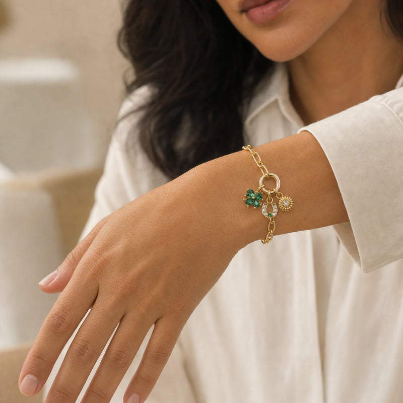 Pulsera de cadena dorada con dijes en una muñeca.