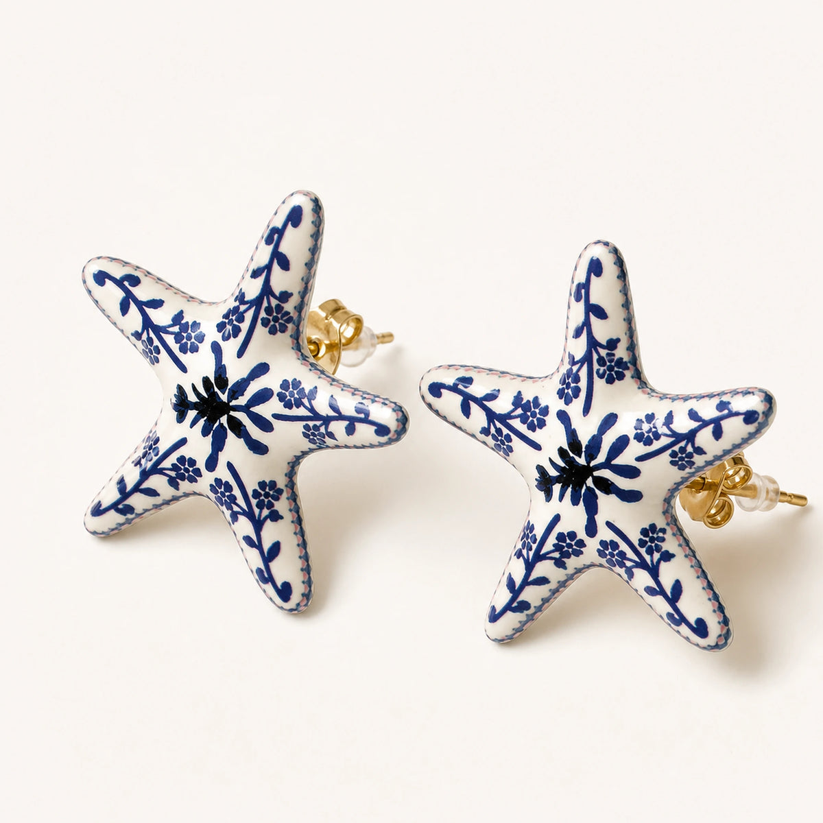 Aretes Jardín Azul: botón de cinco brazos con patrón floral azul sobre marfil.