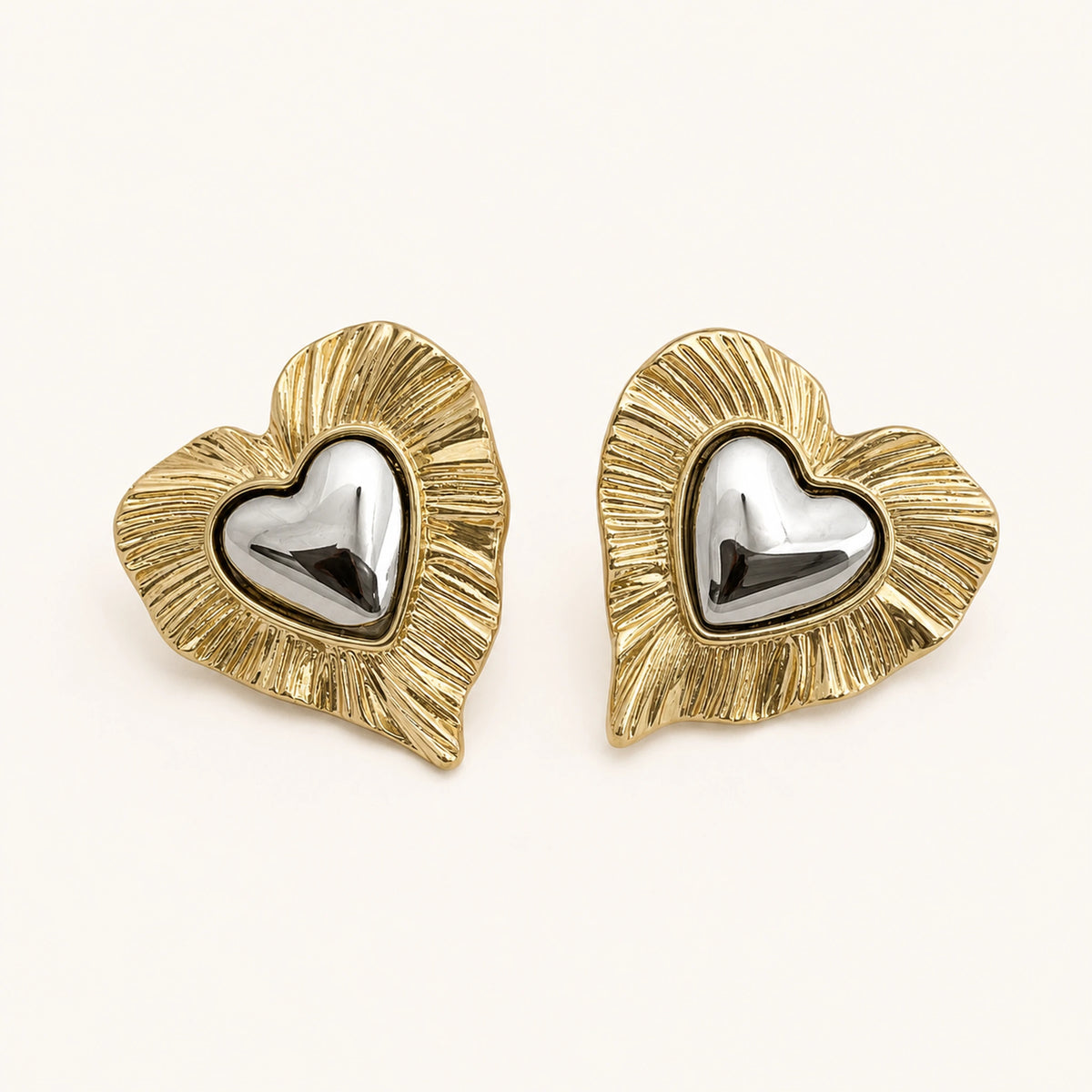 Aretes Doble Corazón: corazón dorado estriado con corazón plateado al centro.